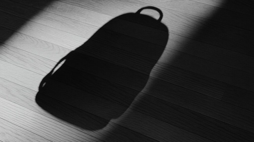 木の床に落ちたバックパックの影が斜めに伸びる。直接写らない“重さ”を光と影だけで感じさせる構図。