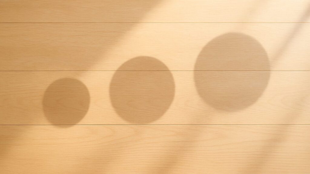 明るい木の床に3つの丸い影が規則的に並び、淡い反射光が広がる。容量や仕分けの整然さを感じさせる構図。